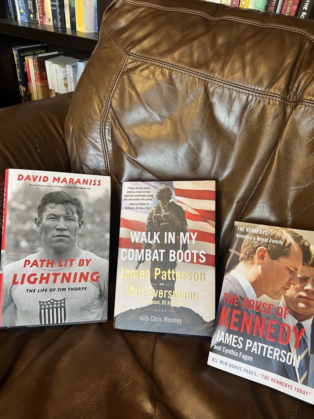 three nonfiction books on a leather chair in front of a bookshelf
