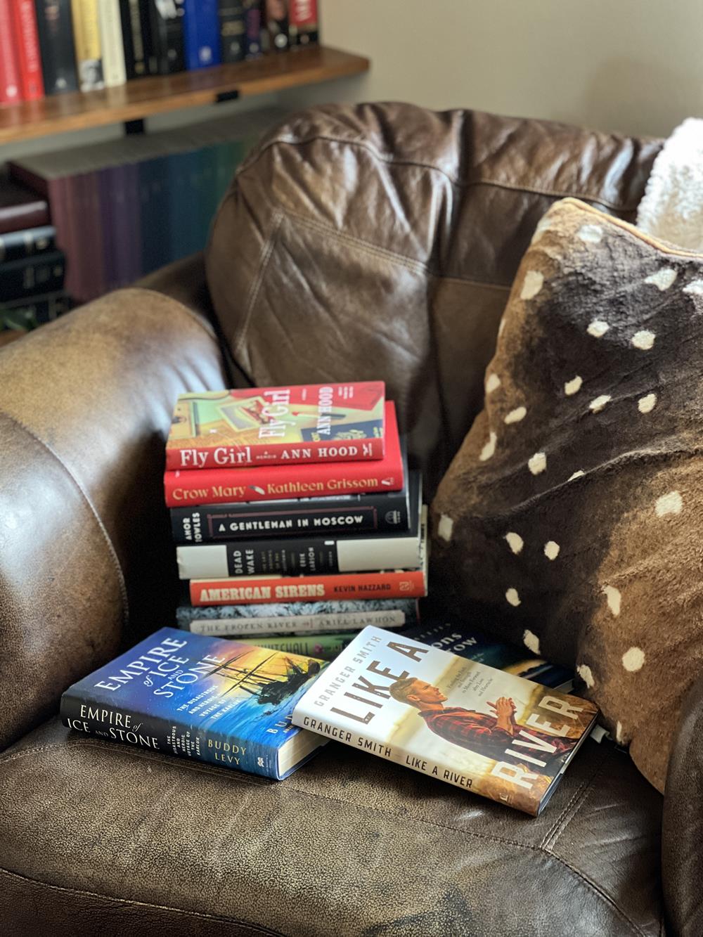 a stack of favorite books of 2023 in a chair next to a pillow and blanket